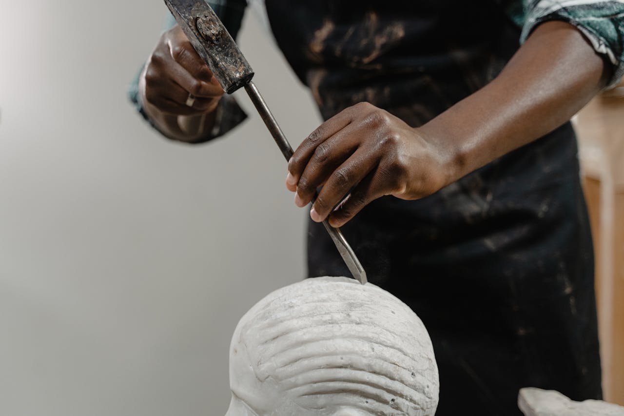 Sculptor chiseling a head sculpture with precision tools. Focus on craftsmanship.